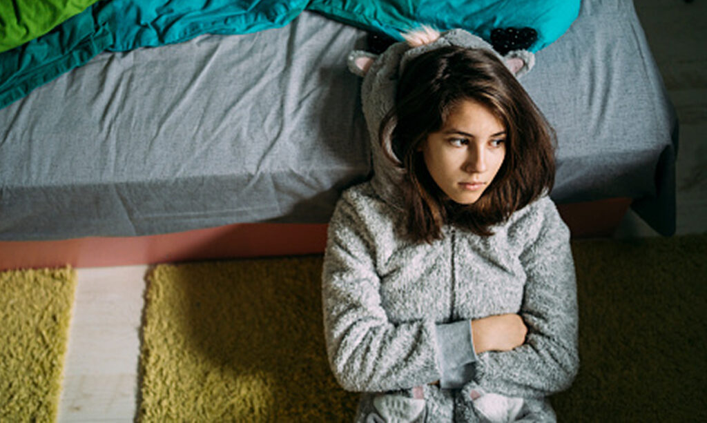 Young teenage girl sitting on the floor of a bedroom looking off screen